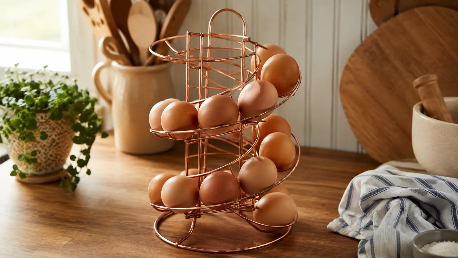 A farmhouse kitchen counter with a spiral egg skelter full of brown eggs in soft morning light